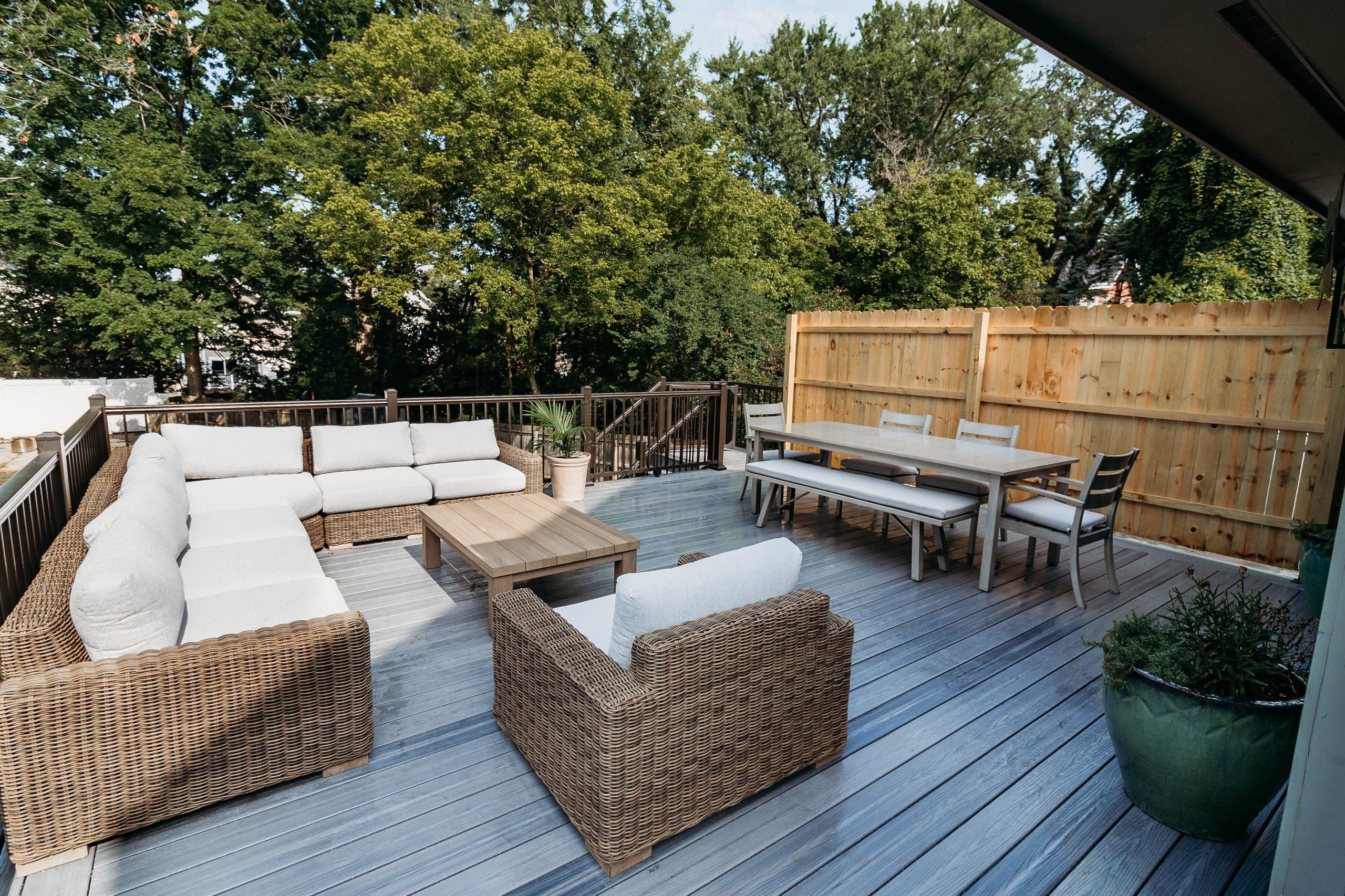 Gray composite deck featuring wicker lounge furniture, a dining set, and black metal railings built by Mueller Remodeling.
