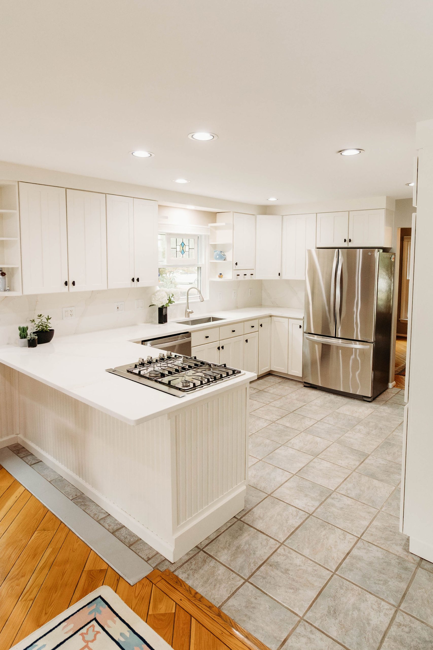 Bright kitchen renovation featuring white shaker cabinets, recessed lighting, and a breakfast peninsula completed by Mueller Remodeling.