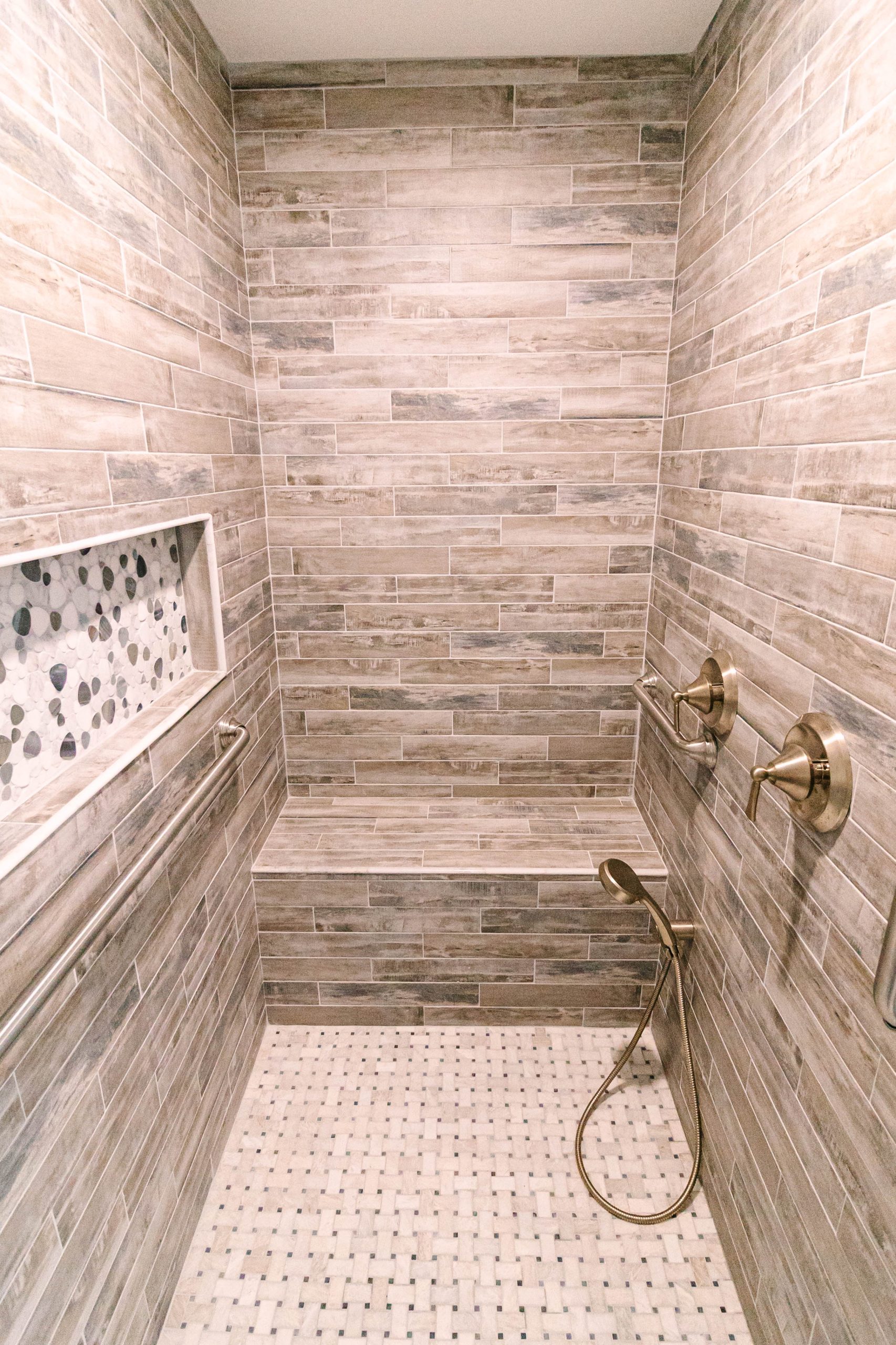 Accessible curbless shower featuring wood-look tile walls and a handheld sprayer built by Mueller Remodeling.