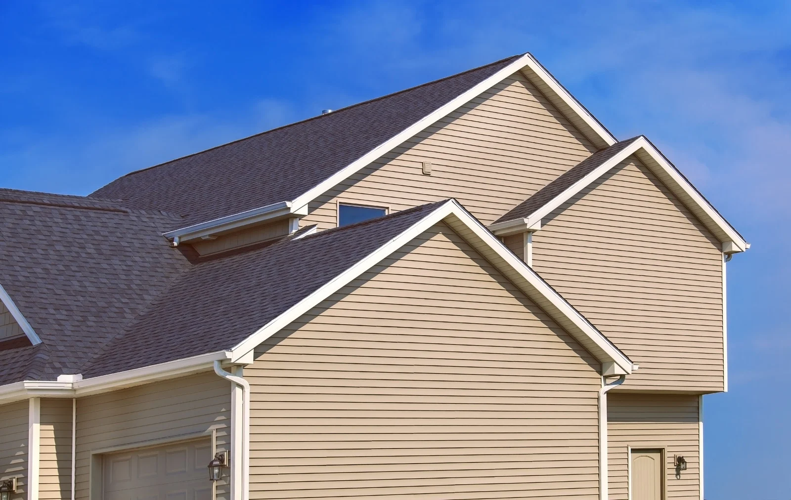 Modern multi-gable home featuring beige horizontal siding, dark asphalt shingles, and clean white trim completed by Mueller Remodeling.