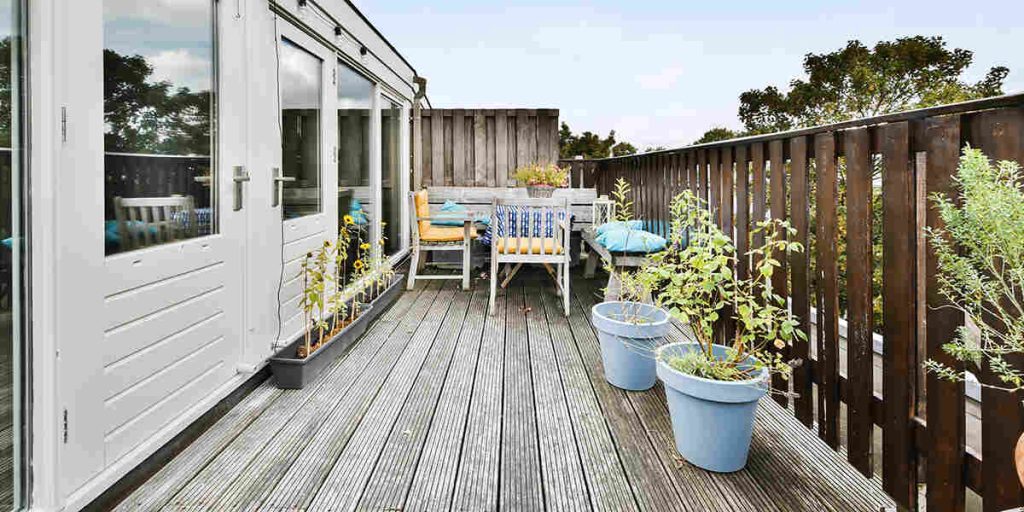 A narrow wooden deck with outdoor seating, potted plants, and a railing demonstrates efficient use of a compact outdoor living space.